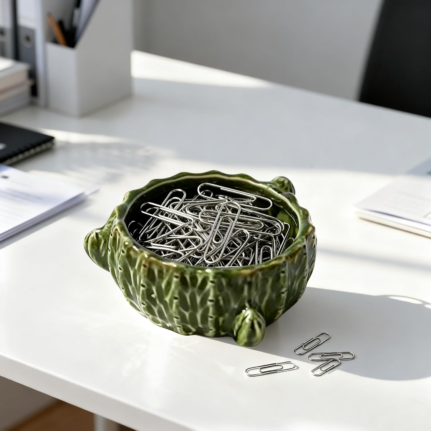 Shows how the decorative bowl can be used to organize and store small office supplies like paper clips, enhancing desk organization and aesthetics.