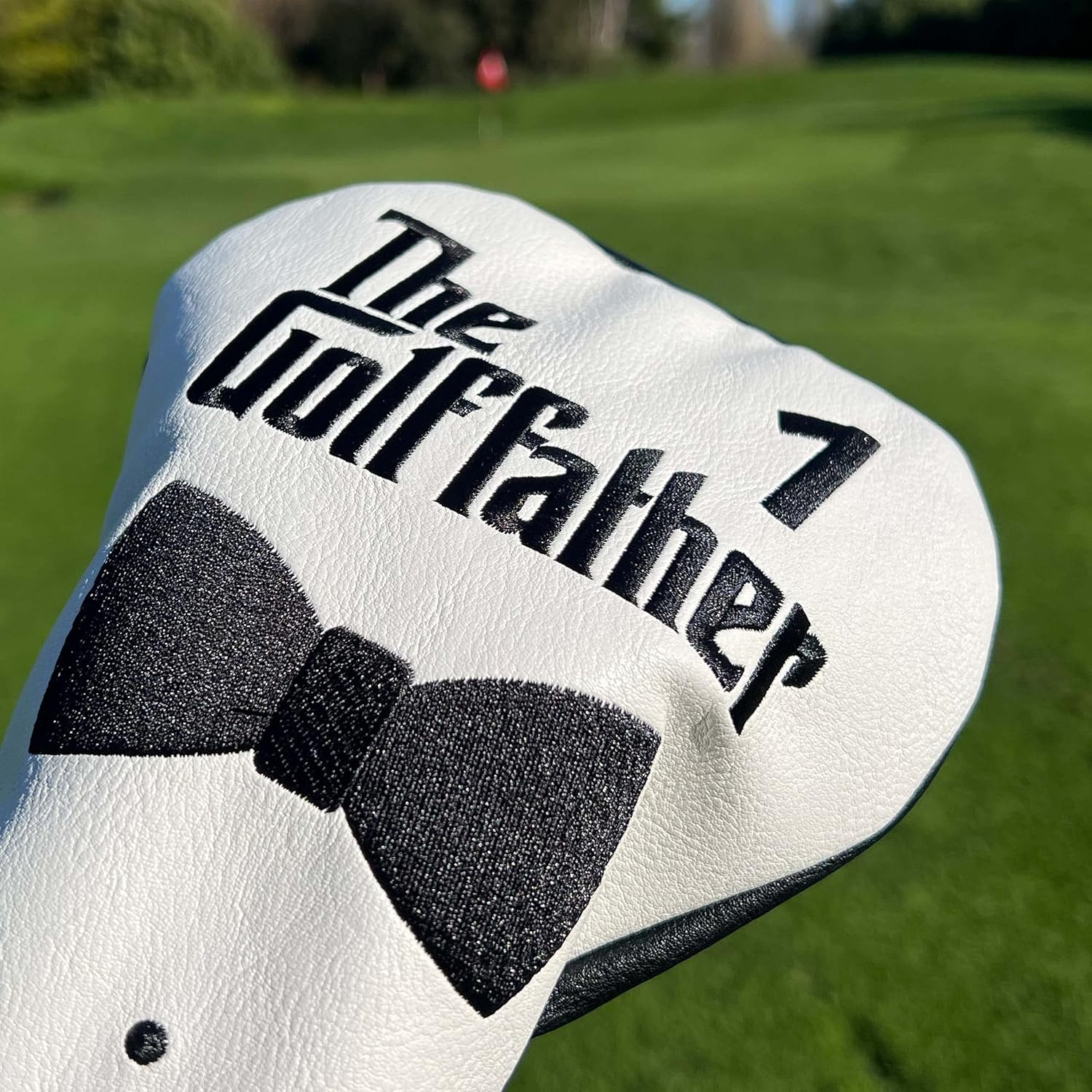 Demonstrates the product in its intended environment on a golf course, showcasing its design and branding Highlights the unique branding of the golf club cover with 'The Godfather' text and bow tie…